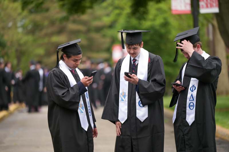 a group of people in graduation gowns and caps looking at their phones