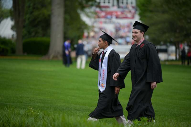 a group of men in graduation gowns walking on grass