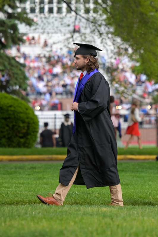 a man in a graduation gown and cap walking on grass