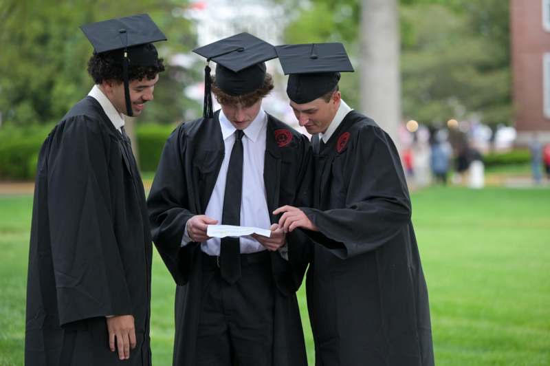 a group of men in graduation gowns and caps looking at a piece of paper