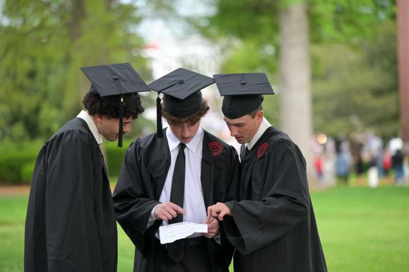 a group of men in graduation gowns and caps looking at a piece of paper