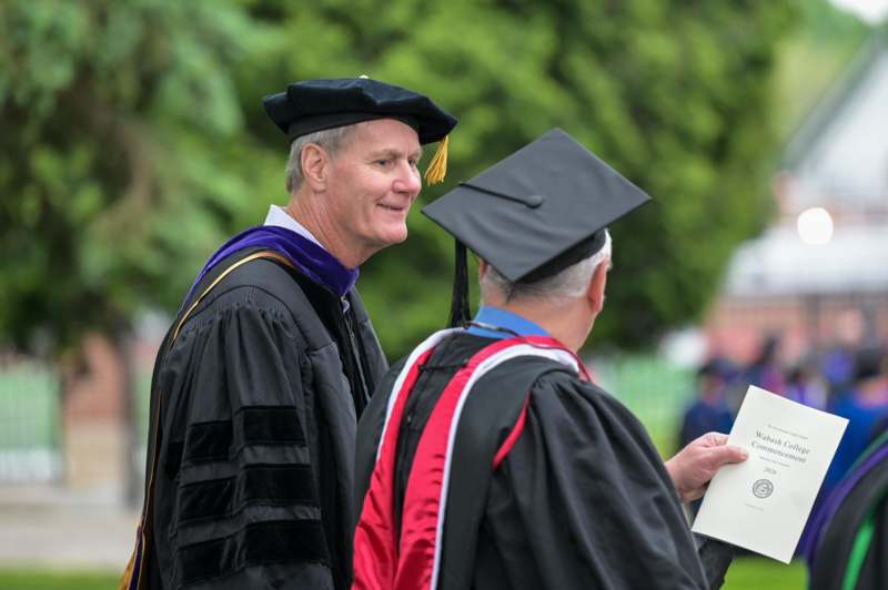 a man in black gown and cap looking at another man in black gown
