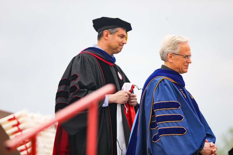 a man in a black robe and a black cap standing next to a man in a black cap