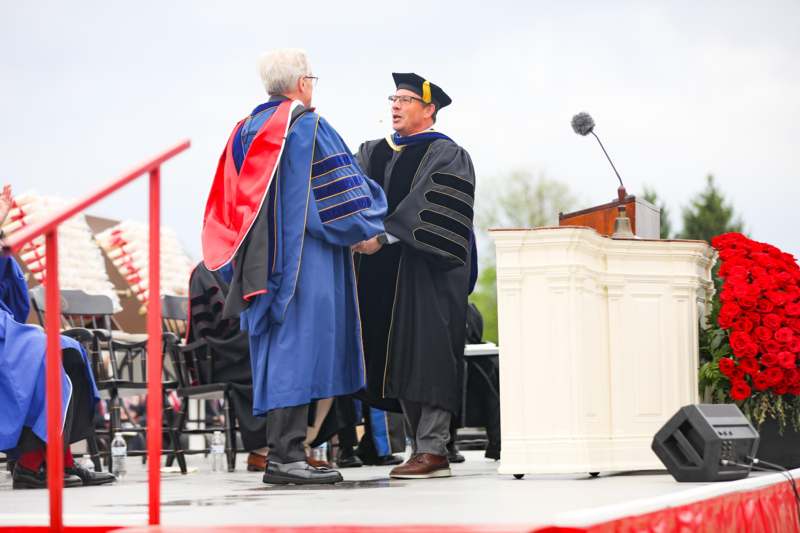 a man shaking hands with another man in graduation gown