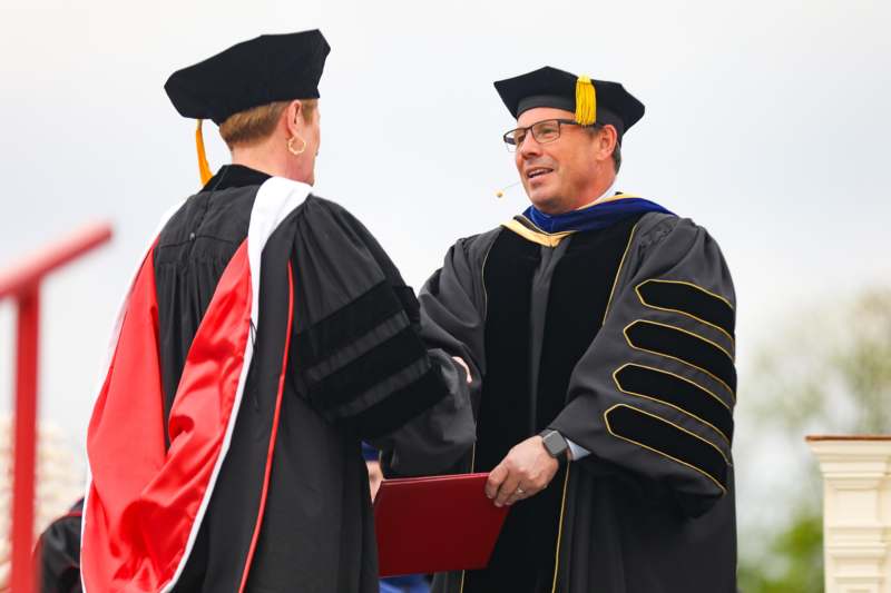 a man and woman in graduation gowns shaking hands