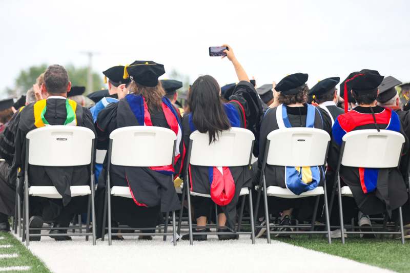 a group of people in graduation gowns and caps sitting in chairs