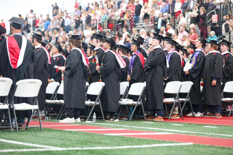 a group of people in graduation gowns and caps standing in chairs