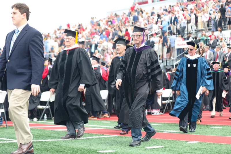 a group of people in graduation gowns walking on a football field