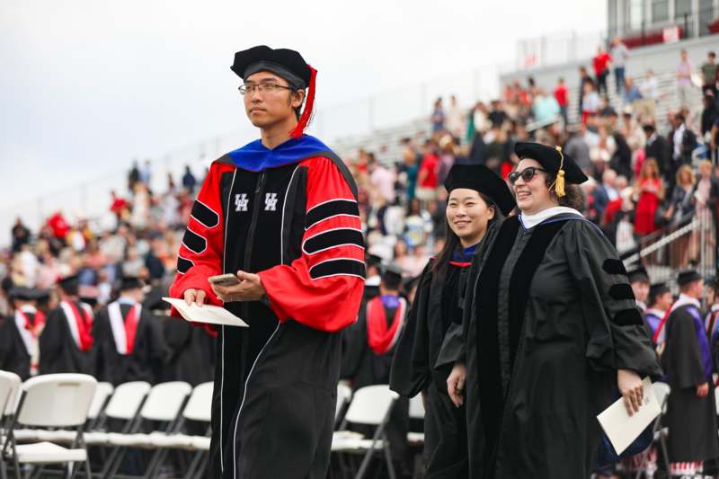a man in a graduation gown and cap standing in front of a crowd