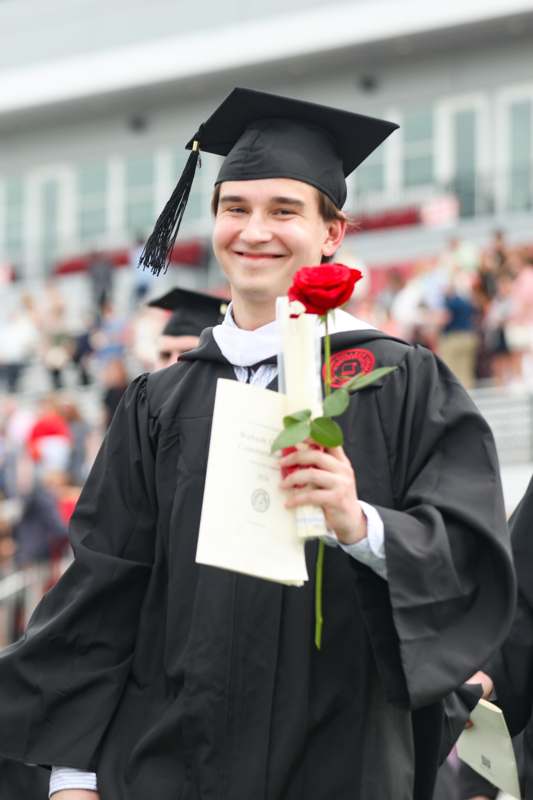 a man in a graduation gown holding a rose and a diploma