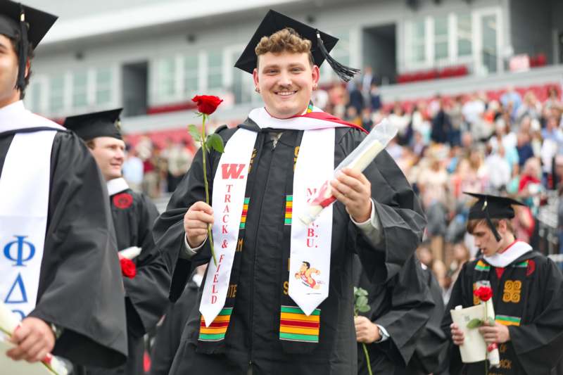 a man in a graduation gown holding a rose and diploma