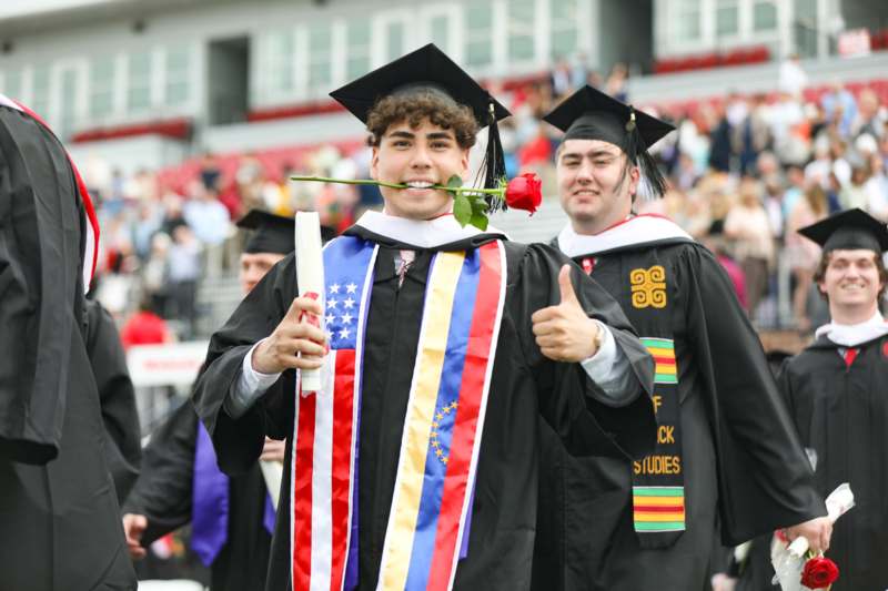 a man in graduation gown holding a rose and giving a thumbs up