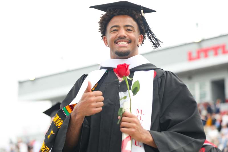a man in a graduation gown holding a rose