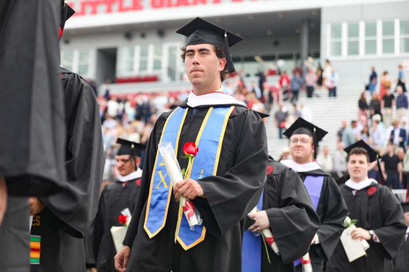 a man in graduation gowns holding a rose