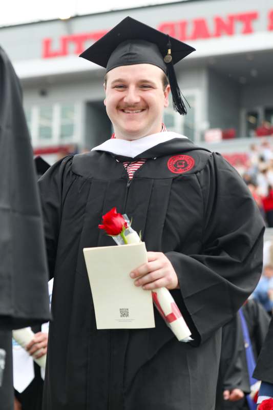 a man in a graduation gown holding a rose and diploma