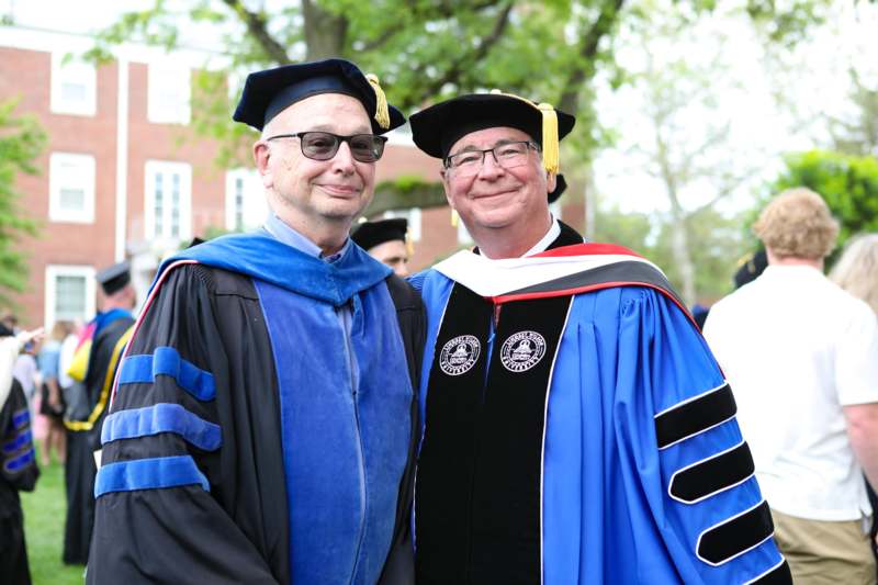 a man in a graduation gown and cap standing next to another man