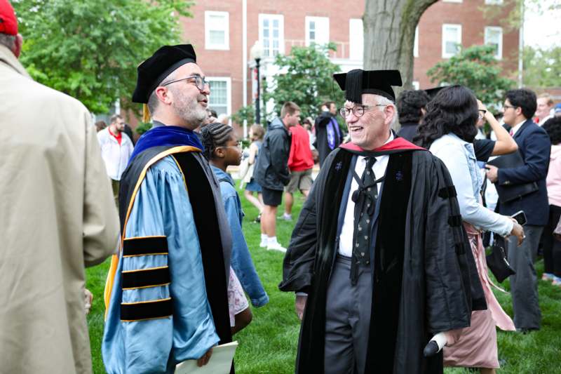 two men in graduation gowns and cap standing in a grassy area