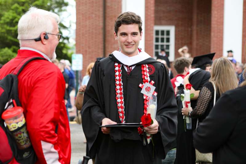 a man in a graduation gown holding a rose and a book