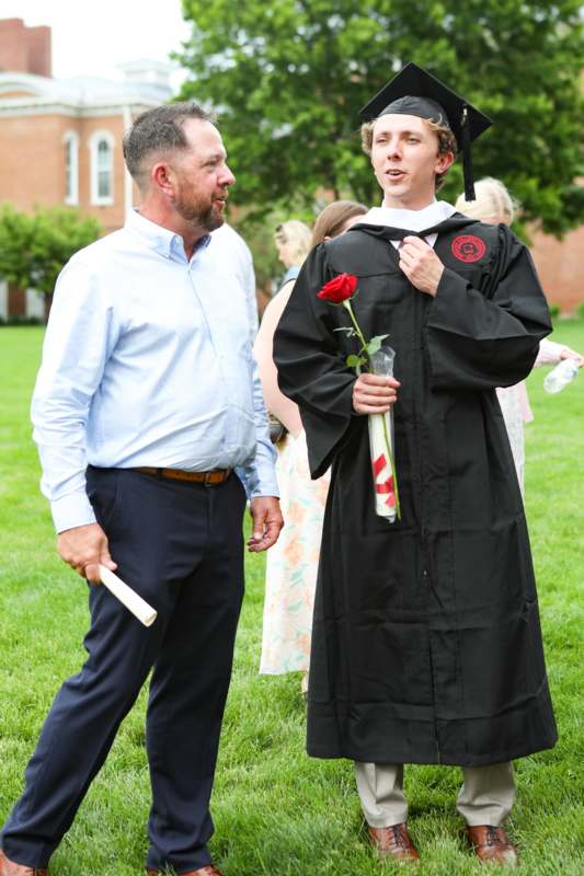 a man in a graduation gown holding a rose and a diploma