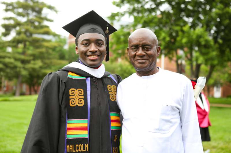 a man in a graduation gown and cap standing next to a man in a white shirt