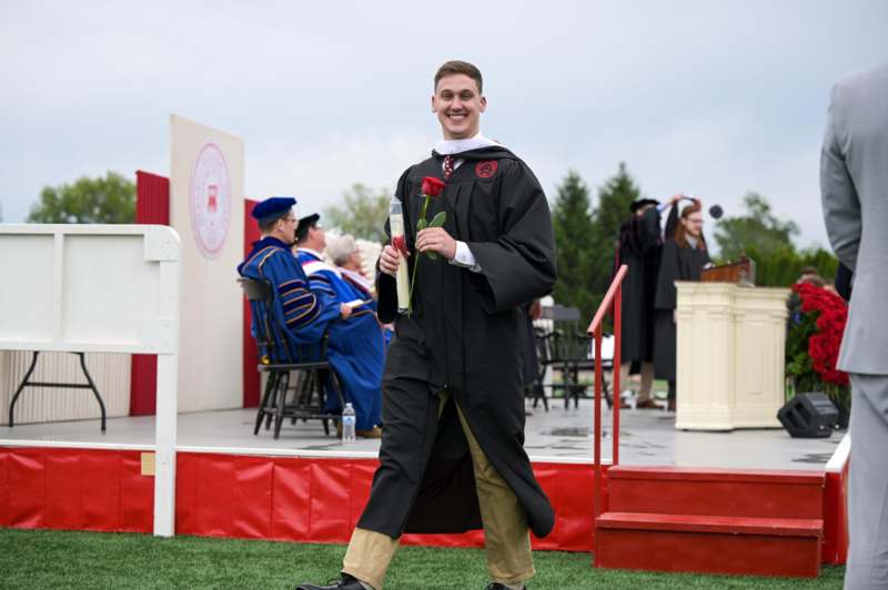 a man in a graduation gown holding a rose and a flower