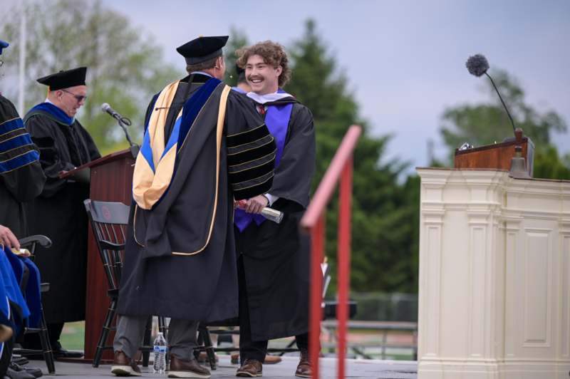 a man in a graduation gown hugging another man in a graduation gown