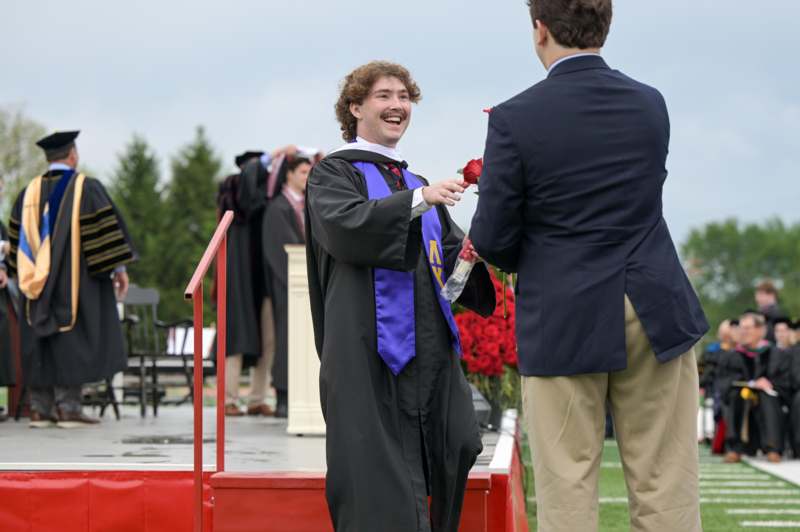 a man in a graduation gown giving a rose to another man