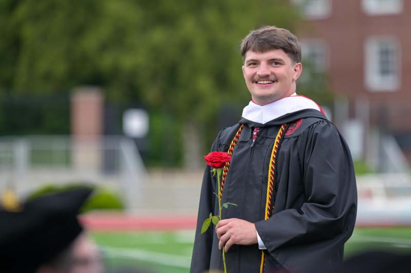 a man in a graduation gown holding a rose