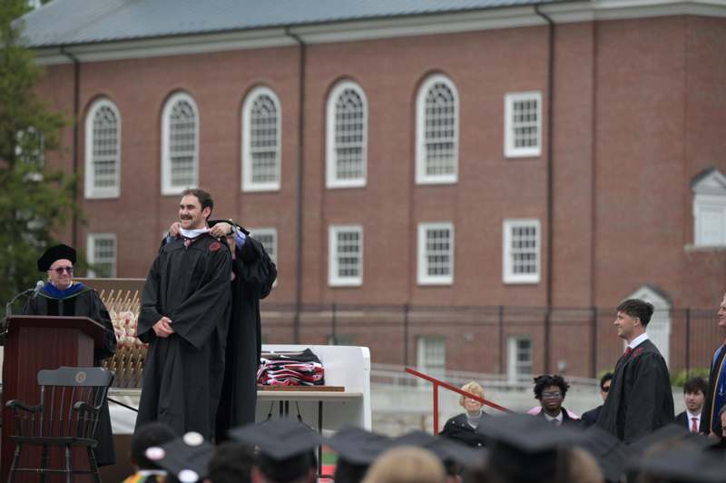 a man in black gowns standing in front of a large brick building