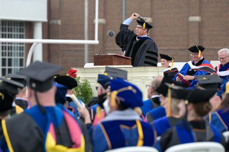 a man in black gown and cap raising his hand up to the podium