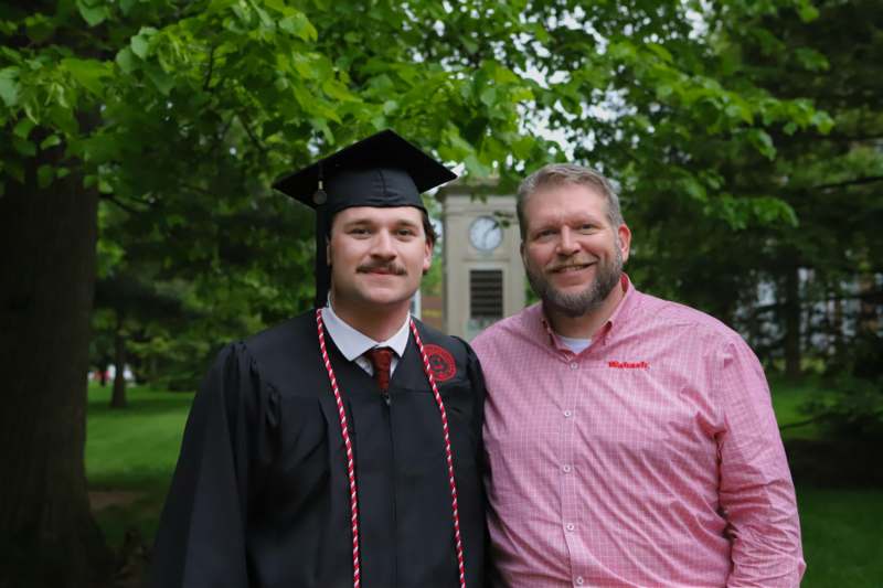 a man in a cap and gown standing next to a man in a red shirt