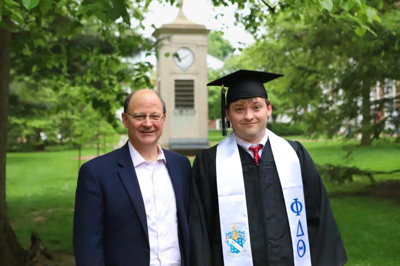 a man in a suit and cap standing next to a man in a graduation gown