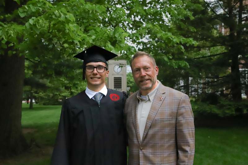 a man in a graduation gown and cap standing next to a man in a suit