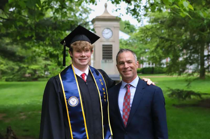 a man in a graduation gown and cap standing next to a man in a suit