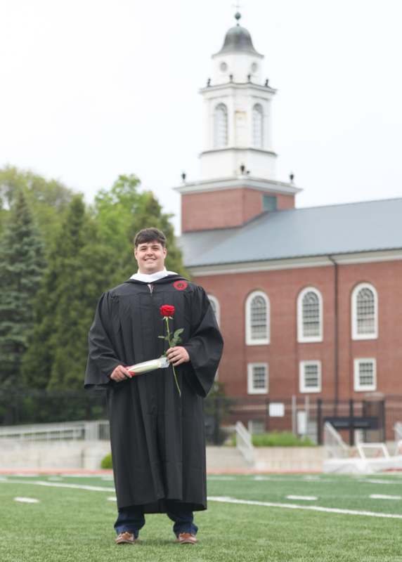 a man in a graduation gown holding a rose