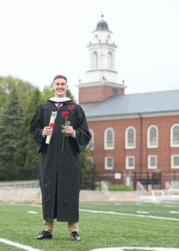 a man in a graduation gown holding a rose and a red rose
