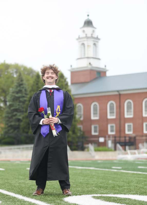 a man in a graduation gown holding a rose and a diploma