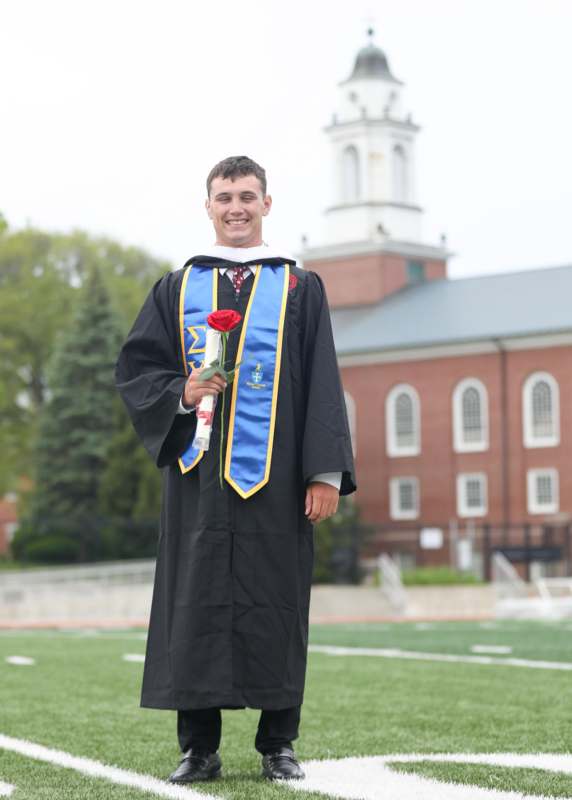 a man in a graduation gown holding a rose