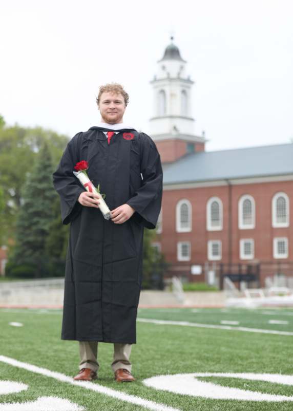a man in a graduation gown holding a rose
