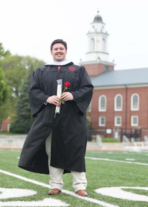a man in a graduation gown holding a rose
