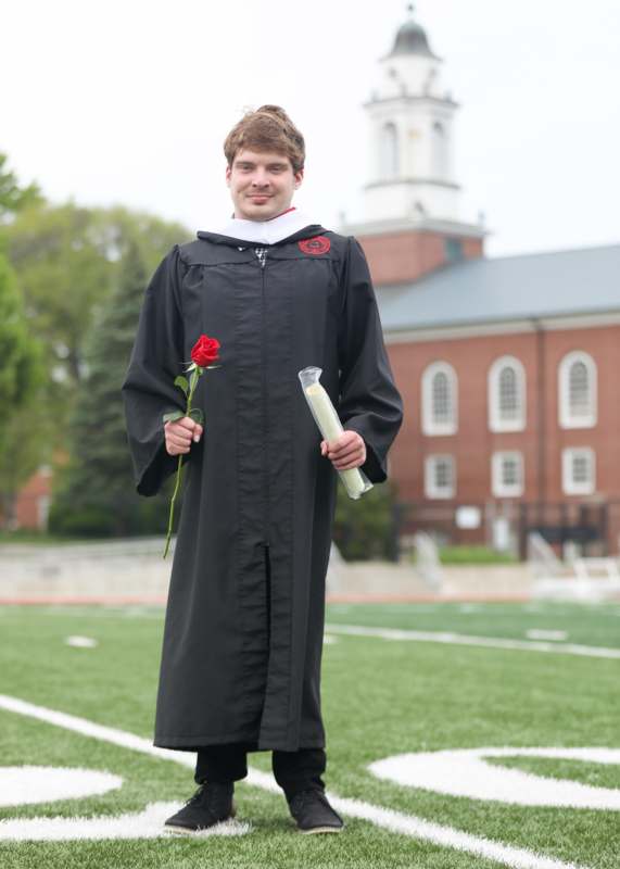 a man in a graduation gown holding a rose and diploma