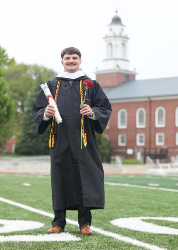 a man in a graduation gown holding a rose and diploma