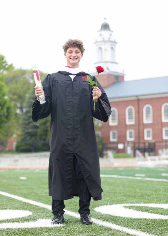 a man in a graduation gown holding a rose and a diploma