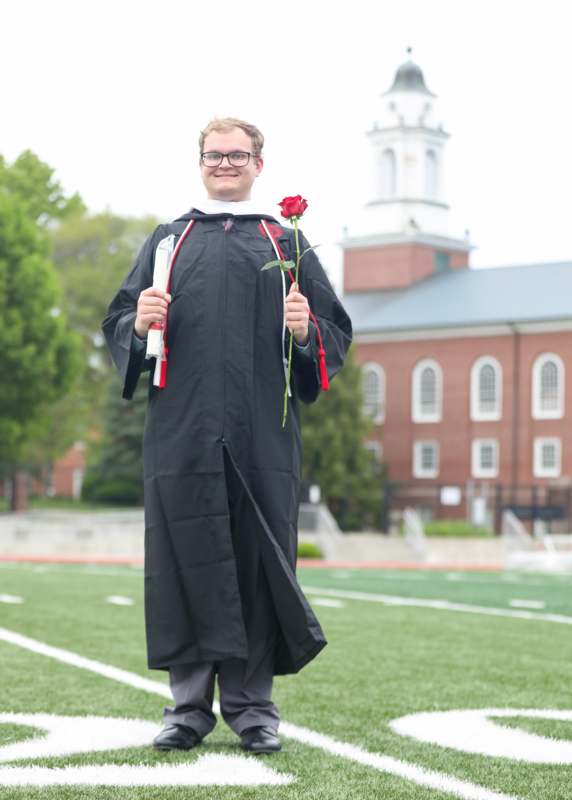 a man in a graduation gown holding a rose and diploma