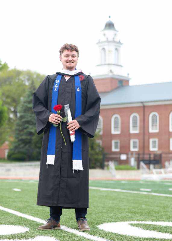 a man in a graduation gown holding a rose and a diploma