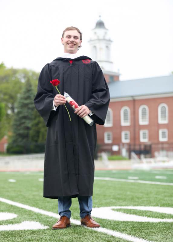 a man in a graduation gown holding a rose