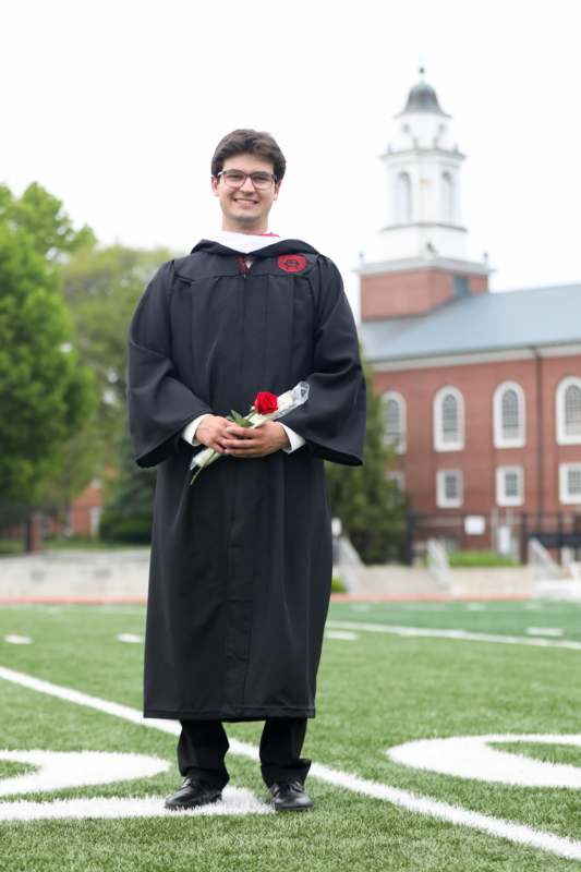 a man in a graduation gown holding a rose