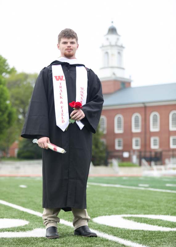 a man in a graduation gown holding a rose and a diploma