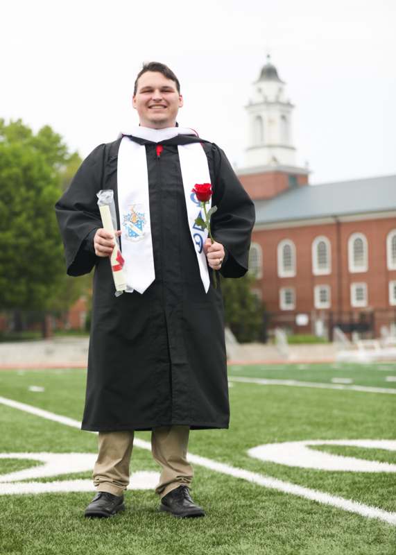 a man in a graduation gown holding a rose and diploma
