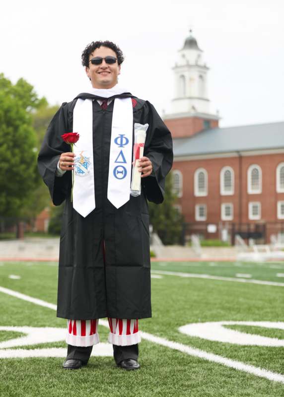 a man in a graduation gown holding a rose and a diploma